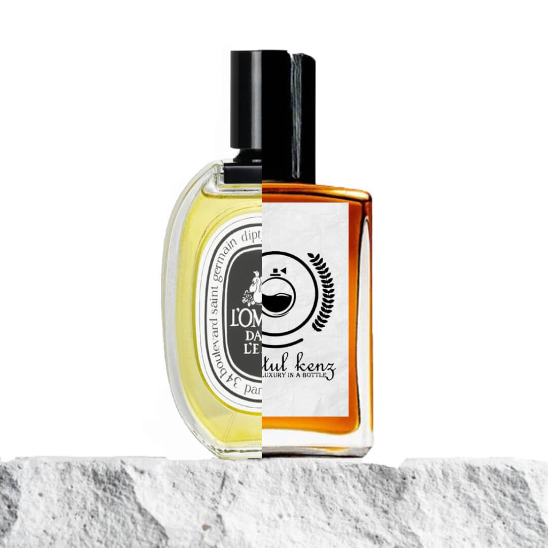 "A split image featuring two perfume bottles displayed side by side."
"On the left, a bottle with yellow liquid and a black label, labeled L’Ombre Dans L’Eau Diptyque, exuding a sophisticated and fresh design."
"On the right, an amber-colored bottle with a white label, representing the Baytulkenz inspired version of L’Ombre Dans L’Eau Diptyque."
"The Baytulkenz bottle features a sleek, warm amber hue, contrasting with the yellow liquid of the original."